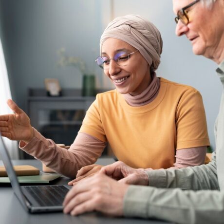 arabic-woman-teaching-senior-man-use-laptop-sitting-desk_23-2149356573